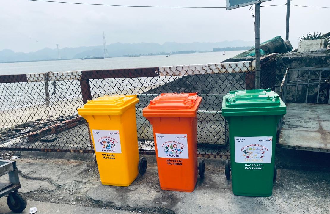 노란색, 주황색, 초록색 대형 쓰레기통이 길가에 차례로 놓여있다.